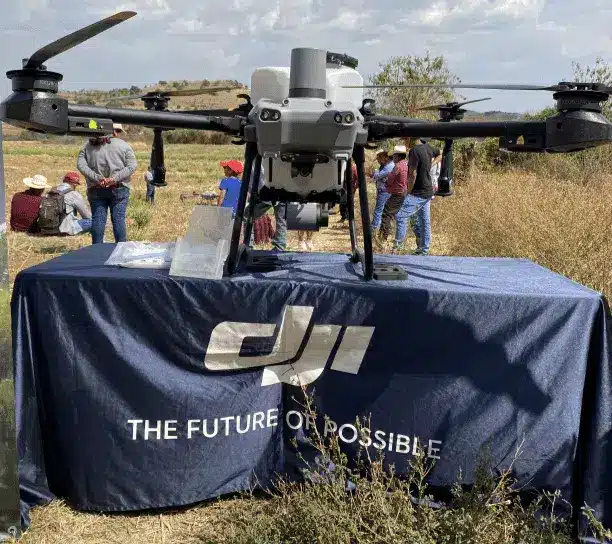 Dron agrícola DJI en exhibición sobre mesa con lona corporativa, durante una demostración en campo como parte del servicio de reparación de drones y refacciones especializadas.