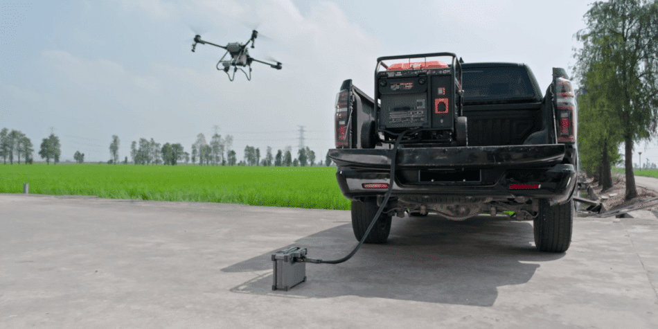agras t25p aterrizando junto a camioneta con un generador y bateria inteligente de dji , hay un campo de cultivo en segundo plano