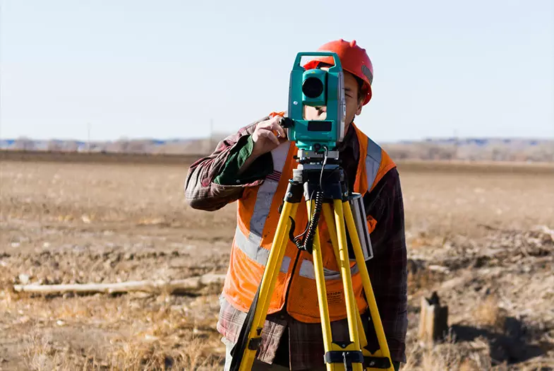 hombre realizando labores de topografia en un terreno desértico